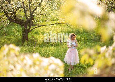 Young attractive girl walks in spring green park enjoying flowering nature. Healthy smiling girl spinning on the spring lawn. Allergy without. Stock Photo