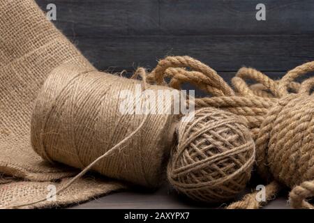 Two spools of burlap threads or jute twine and coil of linen rope on sackcloth fabric in close-up on grey background Stock Photo