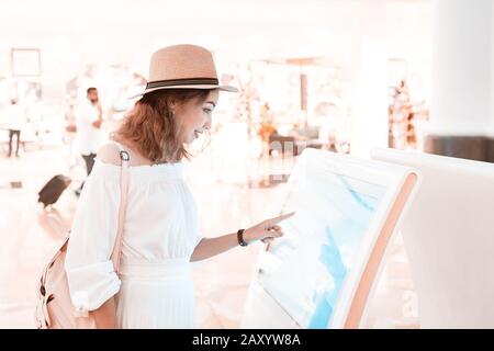 Happy asian girl using an interactive info touchscreen assistant in the shopping Mall. Stock Photo