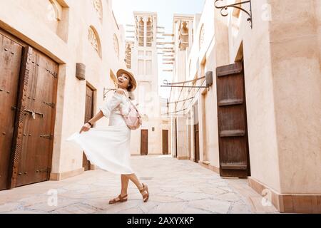 Happy asian girl in white dress walking among narrow streets of old town somewhere in Middle East. Travel destinations and tourism concept Stock Photo