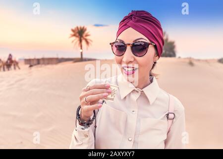 Muslim Woman with turban tasting arabian coffee while having tour and excursion in midlle eastern desert Stock Photo