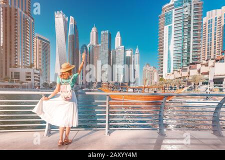 Cheerful asian traveler girl walking on a promenade in Dubai Marina district. Travel destinations and tourist lifestyle in UAE Stock Photo