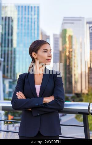 Business woman portrait of young female urban professional businesswoman in suit standing outside office building with arms crossed. Confident successful multicultural Chinese Asian / Caucasian woman. Stock Photo