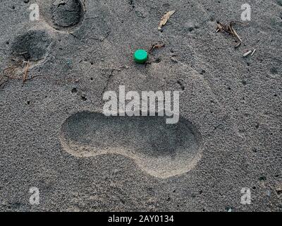 Plastic bottle cork and human footprint on sandy sea ecosystem,microplastics Stock Photo