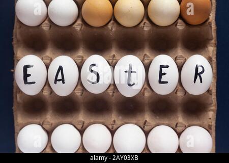 Easter festive eggs in the carton with text. Easter text written on white eggs. Happy Easter, spring festive holidays concept on the colorful background Stock Photo