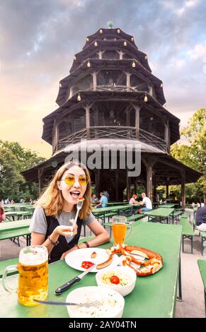 Asian girl eating traditional Pretzel and drinking fresh Bavarian beer in beer garden in Munich. The concept of traditional food festival and tourism Stock Photo