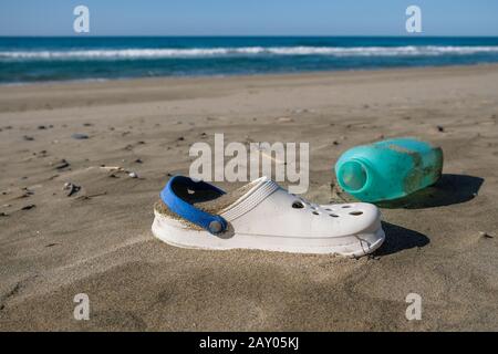Summer slippers and plastic container on wild polluted sea coast ecosystem,italy Stock Photo