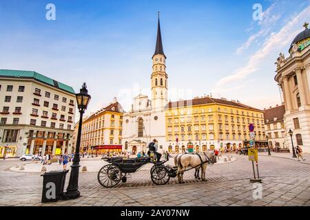 19 July 2019, Vienna, Austria: Panoramic view of St. Michael church on Michaelerplatz square with horse coach and tourists