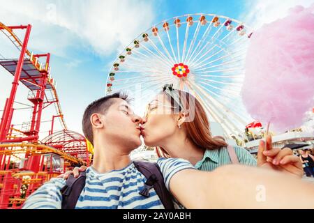 Loving mixed race couple hugging and eating cotton candy and taking selfie during the weekend at the amusement Park. Date and relationship Stock Photo