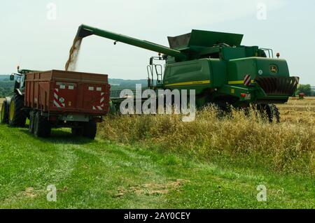 Transferring grain from a John Deere T670 Hillmaster combine harvester to a farm trailer while harvesting wheat near Duras, Lot-et-Garonne, France. Stock Photo