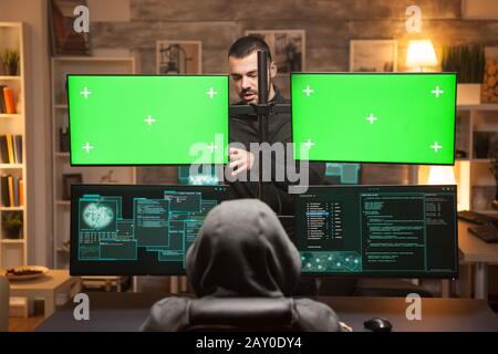Back view team of hackers doying cyber attacks in front of computer with green screens. Stock Photo
