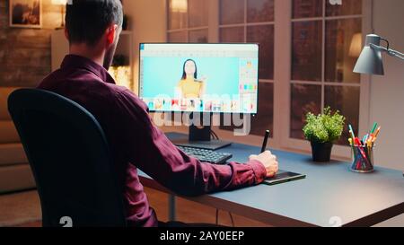 Male photographer editing photos in office at night time using graphic tablet. Stock Photo