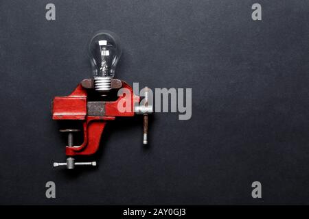 Light bulb clamped in mechanical hand vise on grey background with copy-space. Creative concept Stock Photo