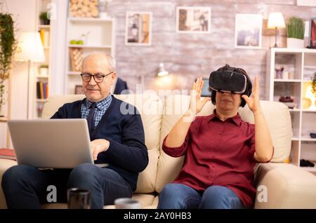 Old elderly retired woman in her 60s experiencing virtual reality for the first time in their cozy apartment Stock Photo