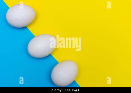 Three Easter holiday flat lay with white egg on a solid bright blue and yellow vibrant background with copy space. Stock Photo