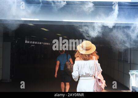 People enjoy a cold water spray at hot summer day near the metro entrance Stock Photo