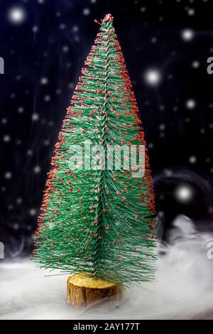 Christmas tree on black background and snowfall, snowstorm and snow on dark. Miniature decorative Christmas tree. Stock Photo