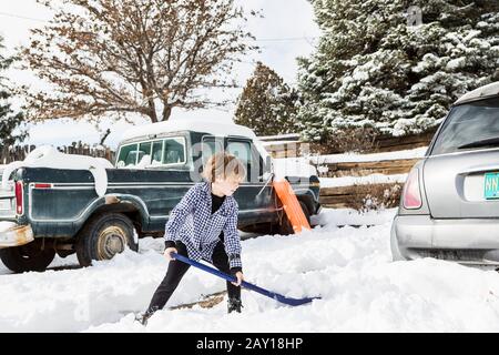 A six year old boy shoveling snow in driveway Stock Photo