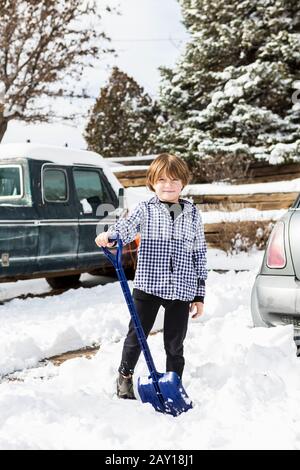A six year old boy shoveling snow in driveway Stock Photo