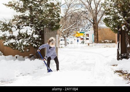 A six year old boy shoveling snow in driveway Stock Photo