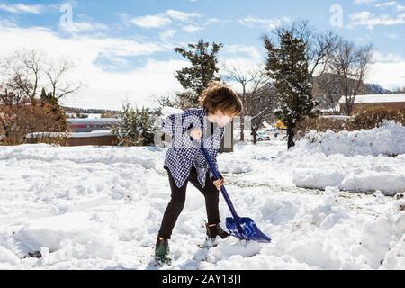 A six year old boy shoveling snow in driveway Stock Photo