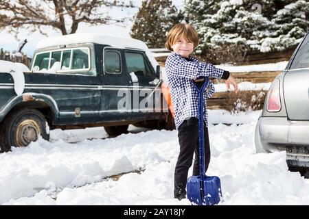 A six year old boy shoveling snow in driveway Stock Photo