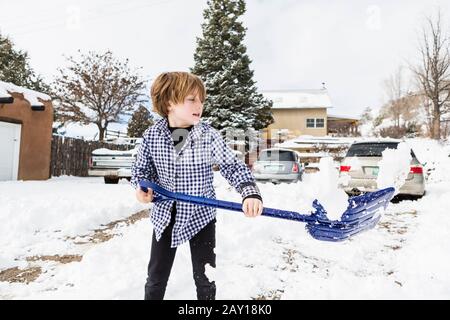 A six year old boy shoveling snow in driveway Stock Photo