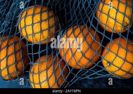 High angle close up of oranges in grey net bag on black background. Stock Photo