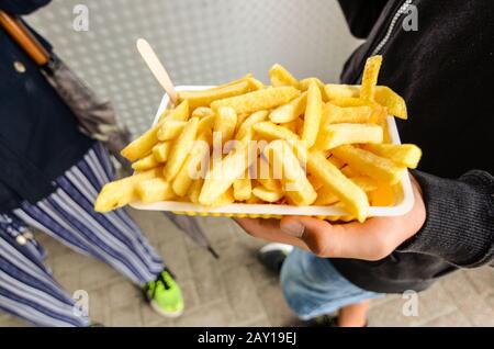 Oosterscheldekering, the Netherlands, August 2019. The main course at a street food kiosk: French fries. One portion is held up with one hand while th Stock Photo