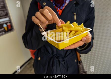 Oosterscheldekering, the Netherlands, August 2019. The main course at a street food kiosk: French fries. One portion is held up with one hand while th Stock Photo