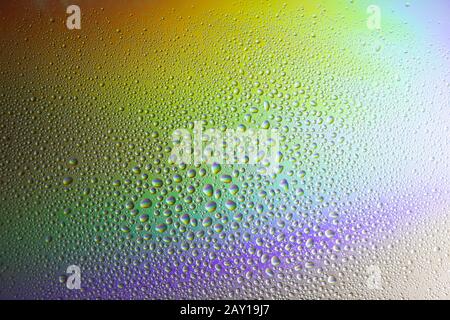 Water drops on glass with colorful rainbow background. Morning dew on the window with a refractive reflection of multicolored sunlight. Stock Photo