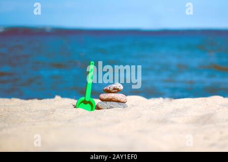 Pretty beach sand toys on dune with gentle waves with sailboat in distance under blue sky Stock Photo