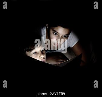 Brother and sister reading light book at night Stock Photo