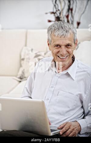 Senior Man Using Laptop Relaxing On Sofa At Home Stock Photo