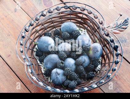 Mixed plum fruits and blackberries in a wooden table on a wooden table. Stock Photo