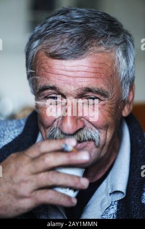 Common elderly man with mustache smoking cigarette and drinking coffee Stock Photo