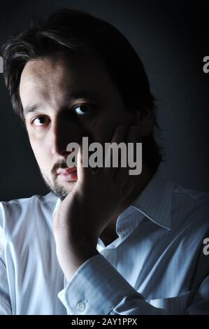 Close-up of young thinking man resting chin on palm, low key Stock Photo