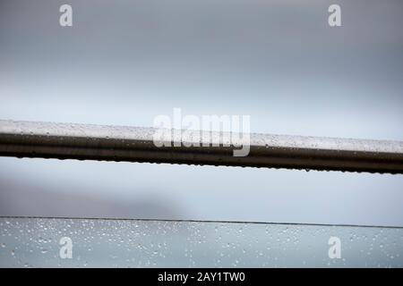 Stainless steel handrail and glass safety panel balustrade close up with raindrops against soft focus blurred overcast grey sky, north wales coast uk Stock Photo