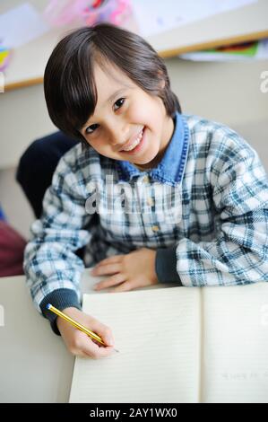 Happy student writing in notebook in school classroom Stock Photo