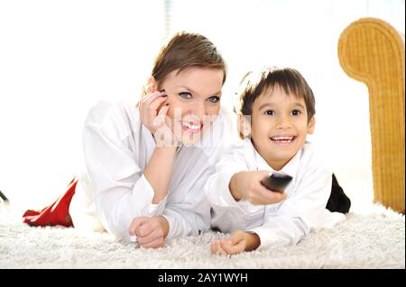 Mom with son lying on floor and watching tv using remote control Stock Photo