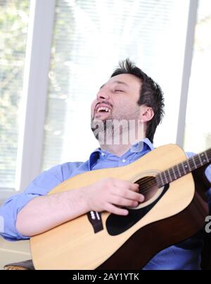 Man playing guitar and singing indoor at sofa Stock Photo