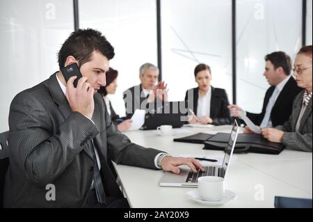 Business man speaking on the phone and typing on laptop while in a meeting Stock Photo