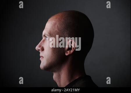 Profile of white bald man in his twenties in dark Stock Photo