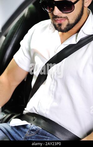 Young man in sunglasses sitting in a car with seatbelt on Stock Photo