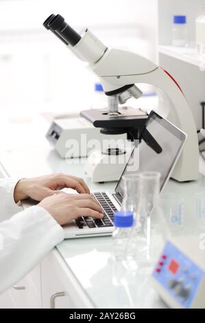 Working in lab with microscope and writing results on laptop Stock Photo