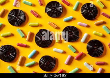 Liquorice spirals and sugar-coated candy arranged in a random pattern on an exotic yellow background in full frame view Stock Photo