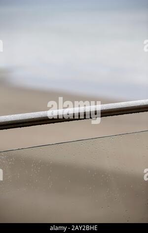 Stainless steel and safety glass balustrade close up with raindrops and soft focus blurred coastal backgound in Abersoch north wales uk Stock Photo