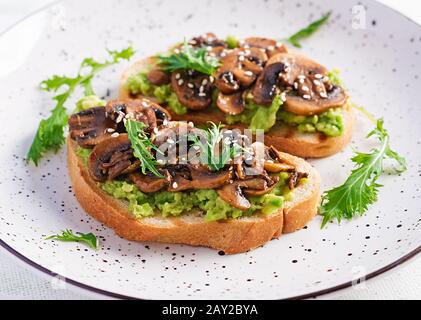 Bruschetta. Sandwich with avocado, fried mushrooms, sesame on a white table. Vegetarian food. Vegan menu. Stock Photo