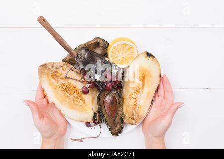 Woman holds a plate with rotten fruits, in which a knife is stuck, Stop wasting food concept, eating stale food. Stock Photo