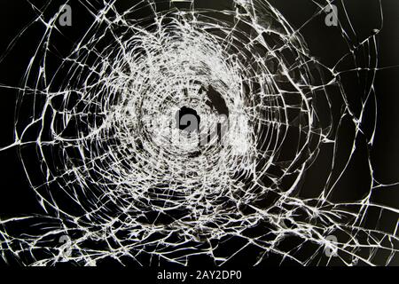 Texture of cracked broken glass with a hole, cracked by impact. Concept shot in the window on a black background for design. Stock Photo